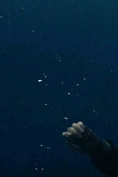 a hand reaching up into the air to catch something in the dark blue water with bubbles