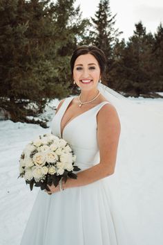 a woman in a white dress holding a bouquet and smiling at the camera while standing in the snow