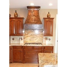 a kitchen with marble counter tops and wooden cabinets, an oven hood over the stove