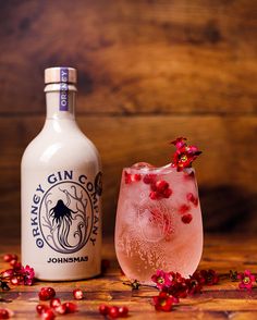 a bottle and a glass filled with pink liquid next to pomegranates