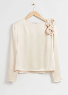 a white blouse with flowers on the shoulder and long sleeves, hanging from a hanger