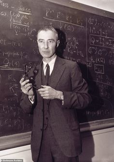 a man standing in front of a blackboard holding a piece of metal pipe and looking at the camera