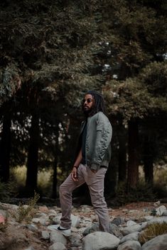 a man with dreadlocks standing on rocks in front of some trees and bushes