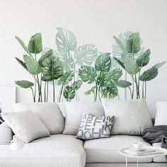 a living room with a white couch and large green leaves on the wall