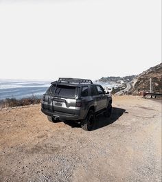 a truck parked on the side of a dirt road next to the ocean and mountains