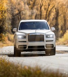 a white rolls royce parked on the side of a road with trees in the background