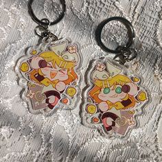 two keychains with cartoon characters on them sitting on a cloth covered tablecloth