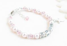 "Pink Pearl Beaded Name Bracelet for Infant, Baby, or Little Girl: This personalized gift features rosaline 5mm Swarovski pearls, 4mm round light rose Swarovski crystals, petite sterling silver alphabet beads, and sterling silver bright daisy spacers. You'll love the sterling silver heart-shaped lobster clasp with a 1/2\" \"Grow with Me\" extender chain. You get your choice of one sterling silver charm: (Cross, silver plated Star of David, Puffed Heart, or Butterfly) All metal components are ste Mother's Day Pink Name Bracelet, Personalized Pink Name Bracelet With Round Beads, Pink Name Bracelet For Birthday, Personalized Pink Round Bead Name Bracelet, Personalized Name Bracelet In Pink, Personalized Pink Name Bracelets, Pink Personalized Name Bracelet As A Gift, Pink Personalized Adjustable Name Bracelet, Personalized Pink Beaded Bracelets With Name