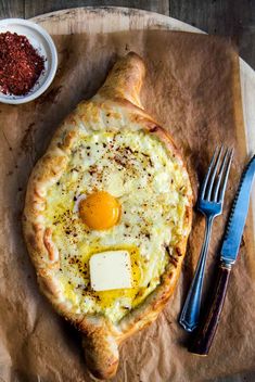 an egg and cheese pizza on a piece of parchment paper with a knife and fork next to it