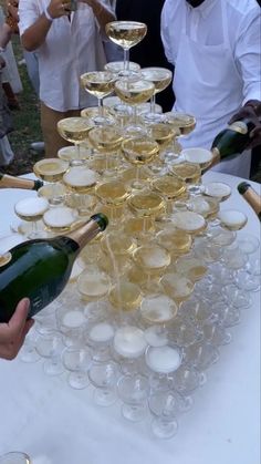 a table topped with lots of wine glasses filled with champagne and people standing behind it