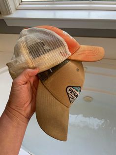 a person holding up a brown and tan hat with an orange brimmed visor