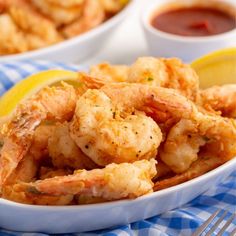 a white bowl filled with cooked shrimp next to lemon wedges and ketchup