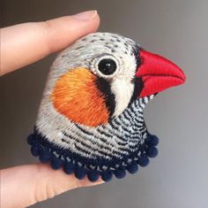 a close up of a hand holding a small bird brooch with red, orange and black feathers