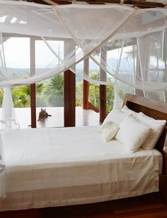 a bed with white sheets and pillows in a bedroom next to a large glass window