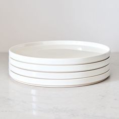 four white plates stacked on top of each other in front of a marble countertop