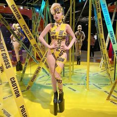 a woman in yellow and black outfit on display at a convention or show with ribbons all around her body