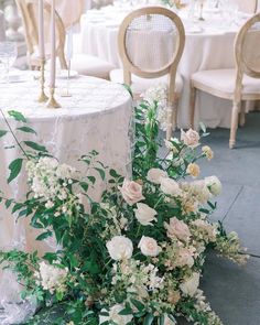 an arrangement of flowers and greenery on a table at a wedding reception, with chairs in the background