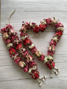 a heart made out of flowers on a wooden table with beads and pearls hanging from it