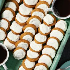 there are many cookies with white frosting on the tray and two cups of coffee