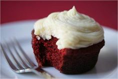 a red velvet cupcake with white frosting on a plate next to a fork