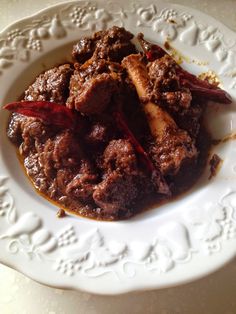 a white plate topped with meat covered in gravy and red peppers on top of it