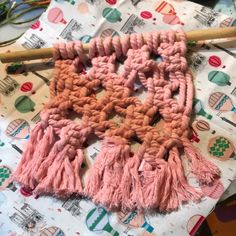 the pink scarf is being made with yarn and wooden sticks on top of it, next to a plant