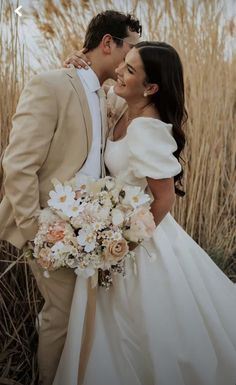 a bride and groom kissing in front of tall grass