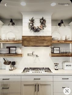 a white kitchen with open shelving and wooden shelves above the stove top is decorated with wreaths