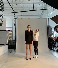 two people standing in front of a white backdrop while one person is taking a photo