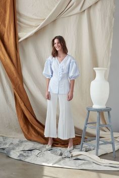 a woman standing in front of a white vase