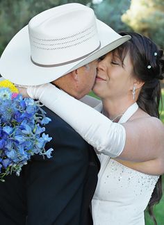 a bride and groom embracing each other in front of some trees with blue flowers on the bouquet