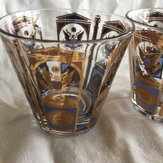 two glass cups sitting on top of a white tablecloth covered table next to each other