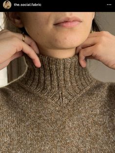 a woman wearing a brown turtle neck sweater with her hands on the top of her collar