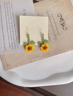 a pair of sunflower earrings sitting on top of a table next to a piece of paper