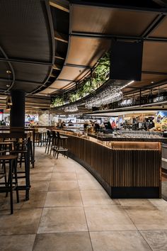 the interior of a restaurant with many tables and stools, lights hanging from the ceiling