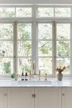 a white kitchen with marble counter tops and gold faucets on the windowsill