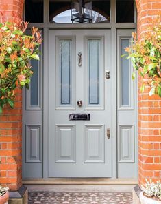 a grey front door with two potted plants on either side and brick wall behind it