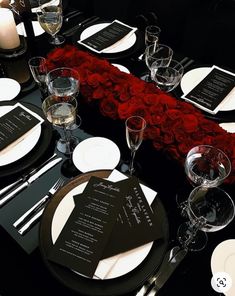 the table is set with black and white plates, silverware, and red roses