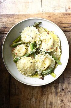 a white bowl filled with mashed potatoes and asparagus on top of a wooden table