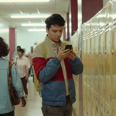 a man standing in front of lockers looking at his cell phone while people walk by