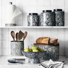 an assortment of kitchen utensils and other items on a shelf in a white tiled kitchen