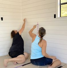 two women are sitting on the floor with their hands in the air and one is holding a measuring tape