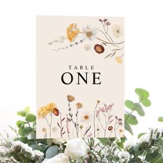 a table sign with flowers and greenery on it that says table one in black lettering