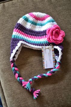 a crocheted hat with a pink flower on the front and blue, green, purple, and white stripes