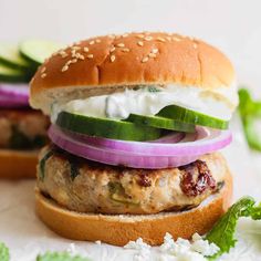 a chicken burger with cucumber, onions and lettuce on a bun