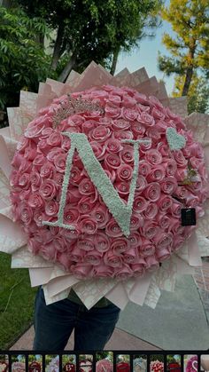 a woman holding up a giant pink rose bouquet with the letter n in it's center