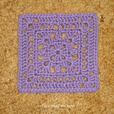 a purple crocheted square with hearts on it sitting on top of a carpet