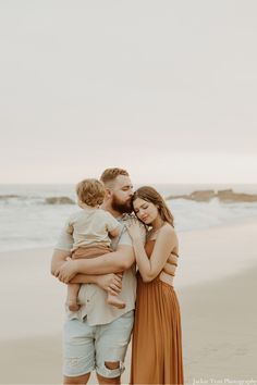 a man and woman are holding their son on the beach while he is kissing his forehead