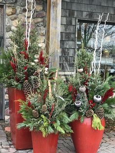 three red planters filled with pine cones and evergreens in front of a house