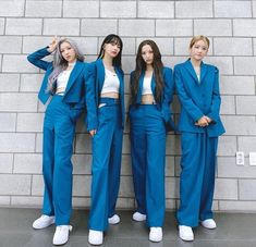 three girls in blue suits standing next to a brick wall and posing for the camera